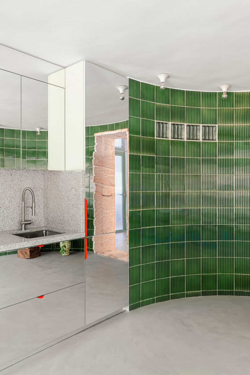 Modern kitchen detail with vertical green tiles, a mirrored cabinet, and a stainless steel sink.