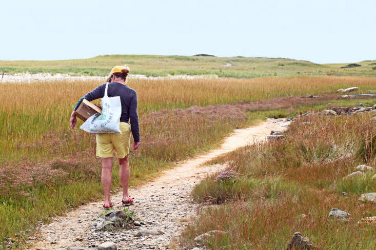 A woman walking along a rocky coastline looking for materials.