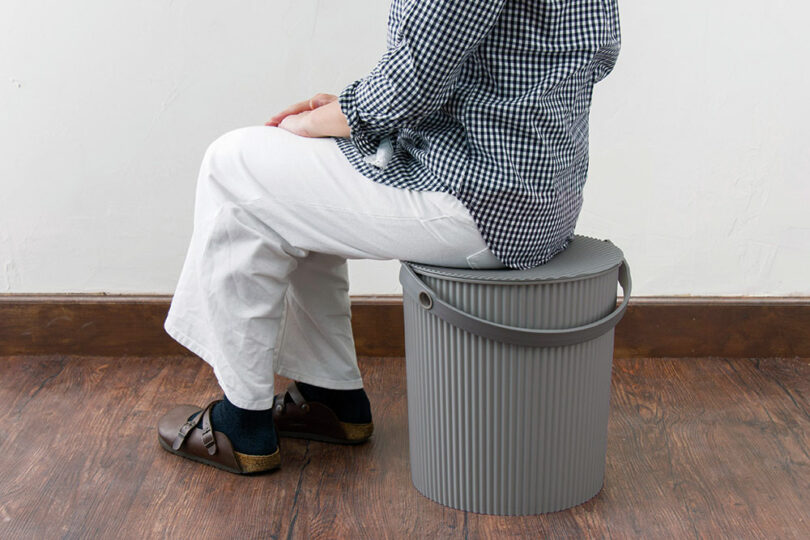 A person sitting comfortably on a grey Hachiman bucket, demonstrating its strength as a seat.