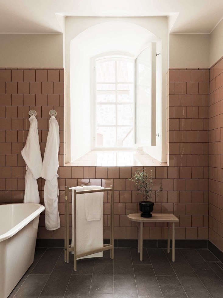 A collapsible wooden towel rack positioned against pink wall tiles at the Wanås Hotel in Sweden.