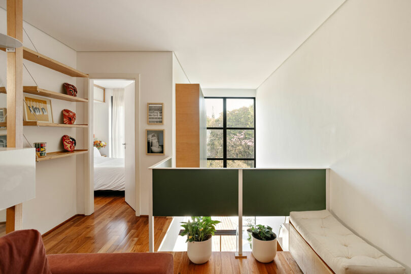 Upstairs hallway with wooden floors, a green partition, and a view into a sunlit bedroom.