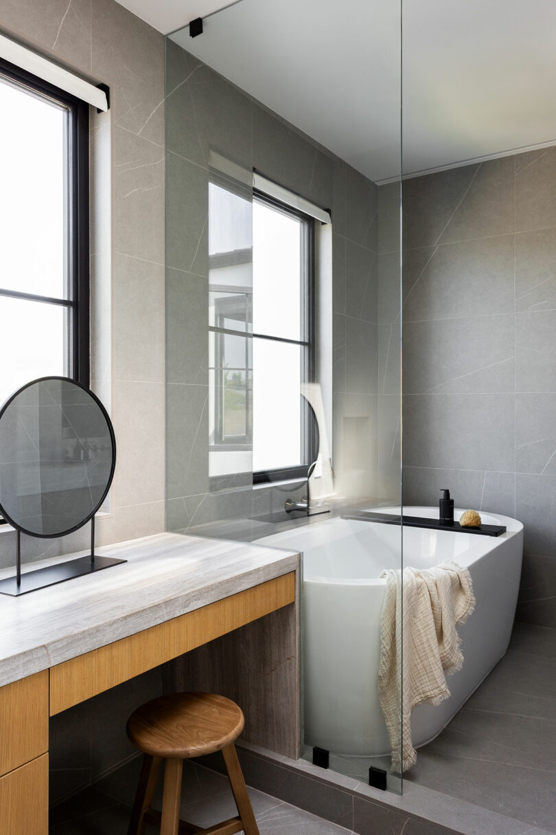 Modern bathroom with a freestanding bathtub, wooden vanity, and large windows letting in natural light.