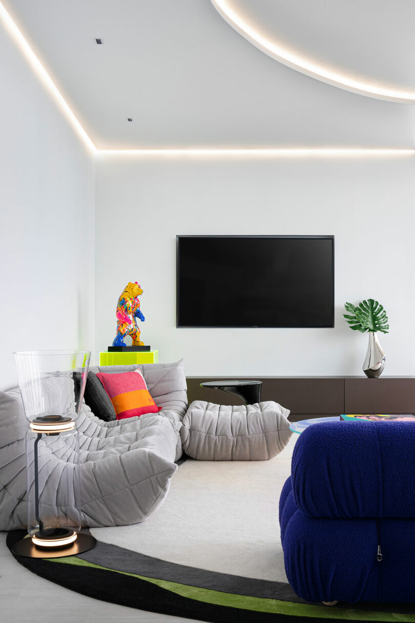 Modern living room featuring a curved gray sofa, a blue chair, and a ceiling with matching curved light recessed designs.