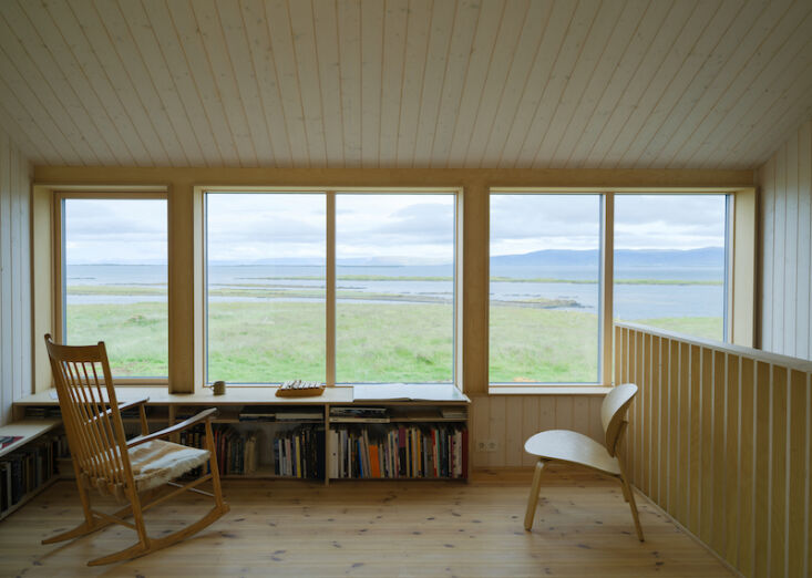 A mezzanine living area with plywood walls and a window bench overlooking the sea.