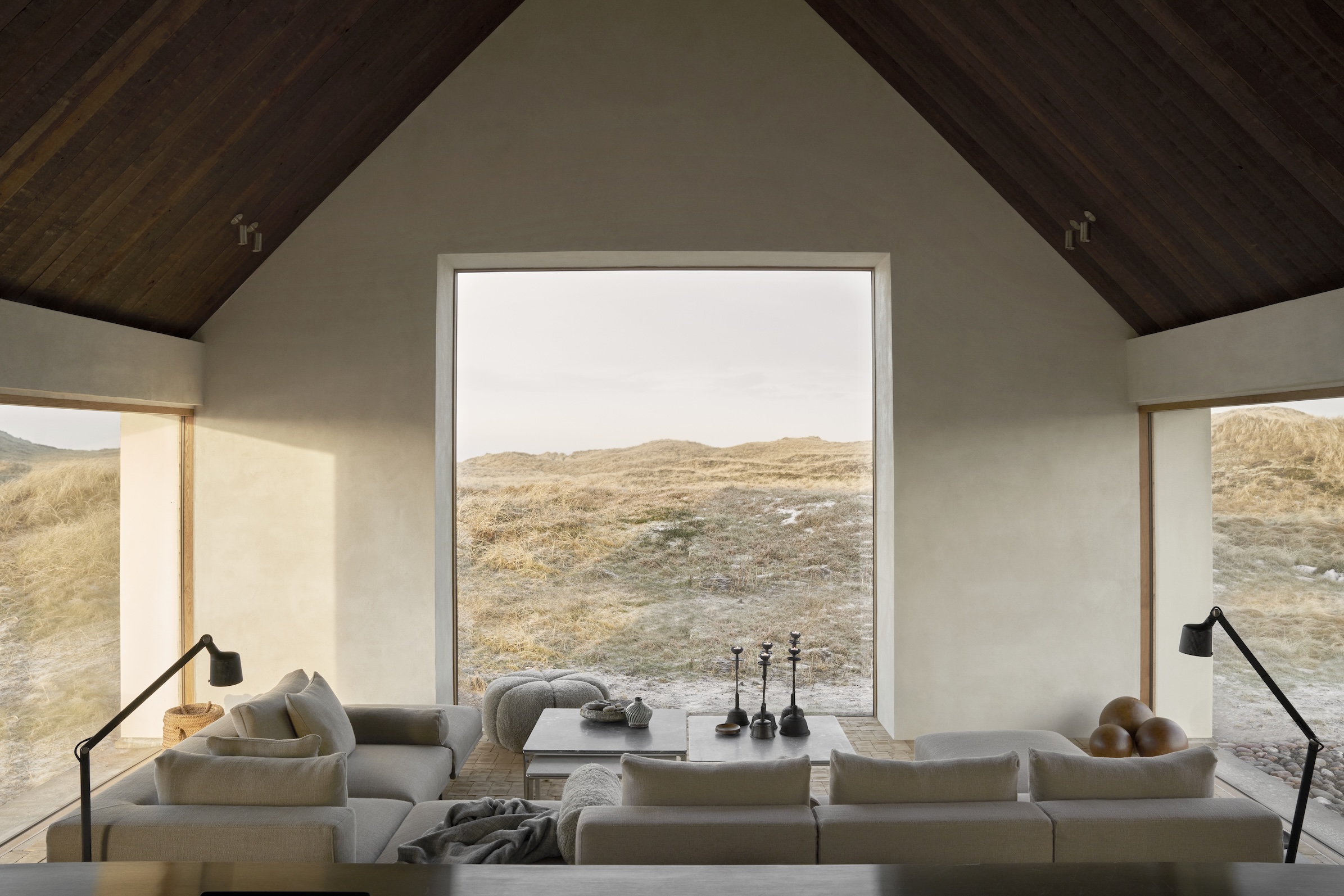 A modular grey sofa in a minimalist living room with a large window looking out onto the dunes.