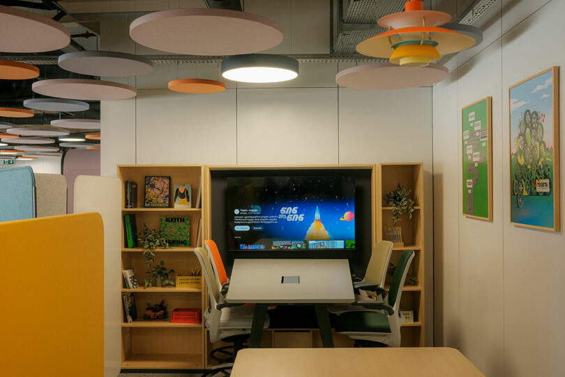 A modern meeting room with a wooden table, ergonomic chairs, and a screen displaying a presentation.