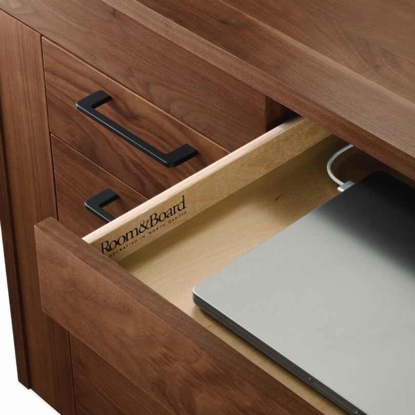 A partially open desk drawer revealing a laptop stored inside, highlighting the Room & Board branding.