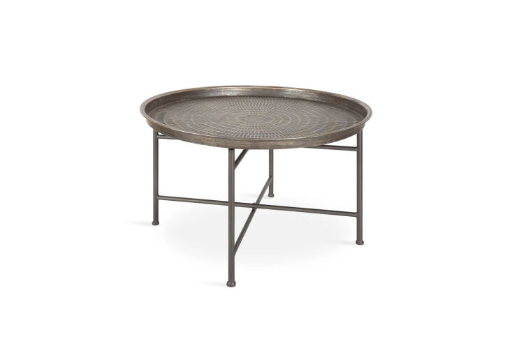 A round hammered metal tray table on a gold-finished stand.