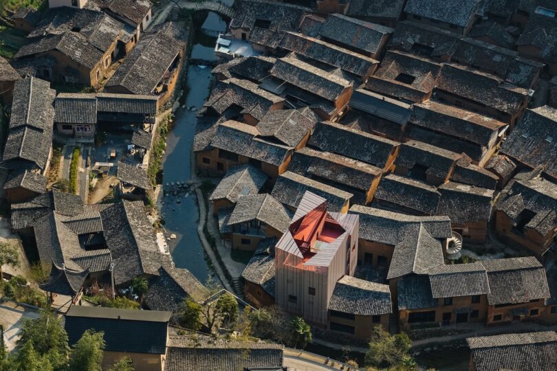 Aerial view of a traditional village with a canal, featuring the modern light-colored museum building among older structures.