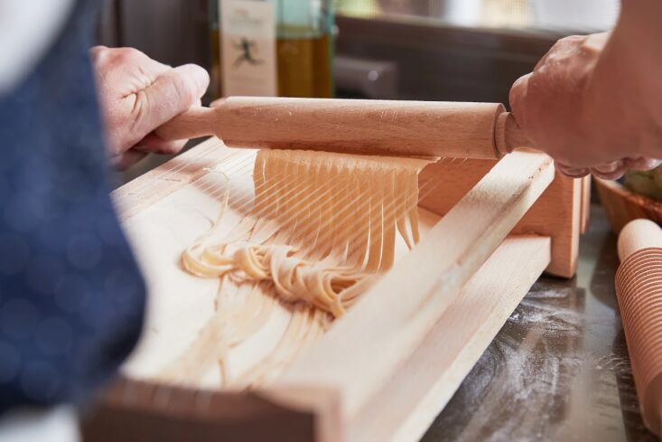 A cook using a wooden Chitarra with iron strings to cut fresh pasta dough.