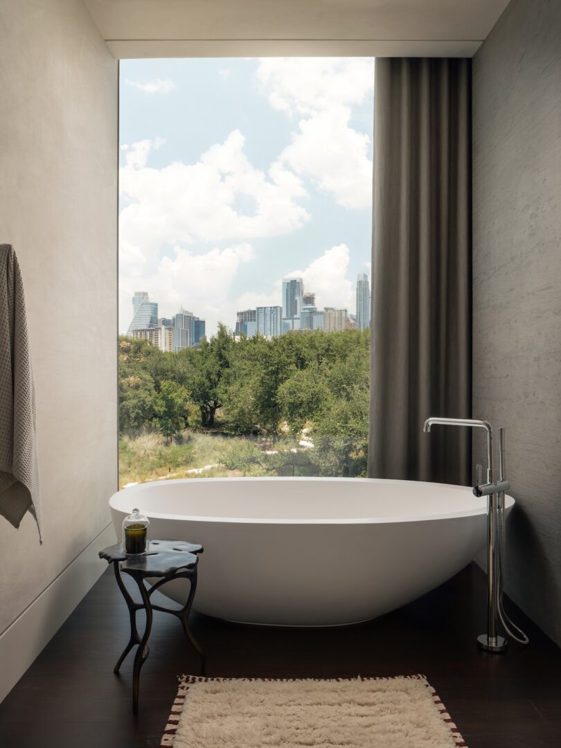 A luxury freestanding bathtub positioned next to a window overlooking the Austin city skyline.
