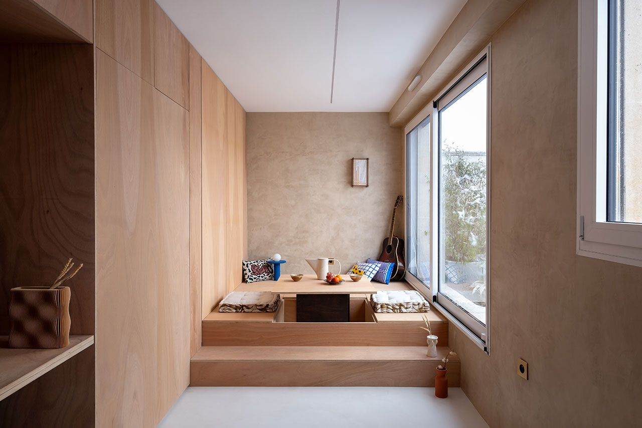The interior of a minimalist Parisian studio with warm wood surfaces and a large window.