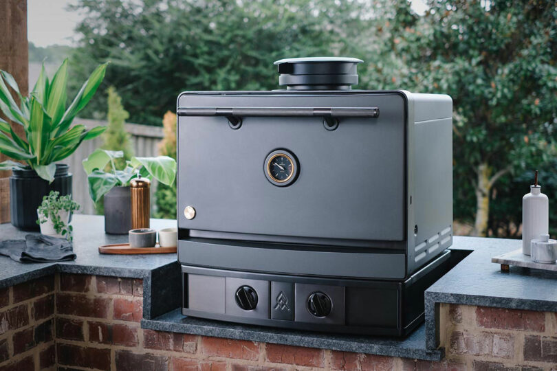A black Emberhaus oven permanently installed on a brick outdoor kitchen counter.
