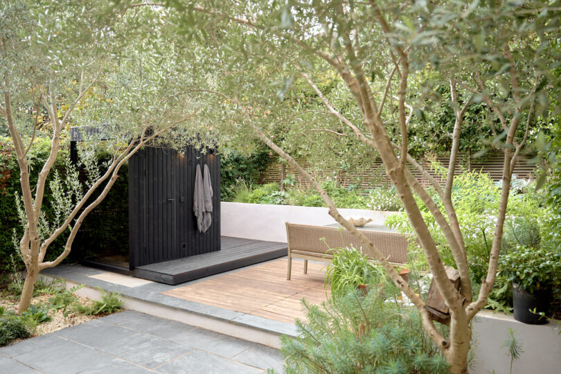 A compact black outdoor sauna positioned on a wooden deck in a garden.