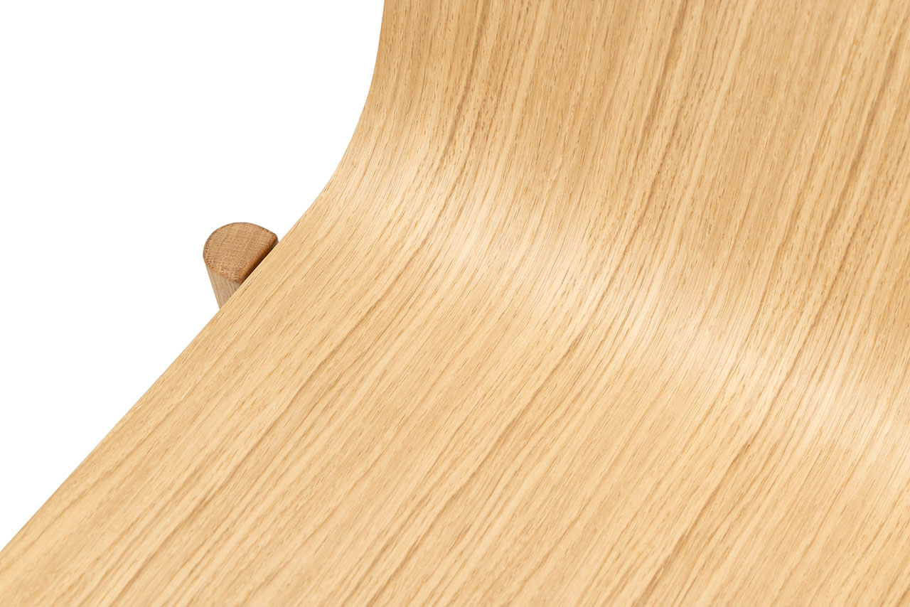 Close-up of a light wood chair showing the smooth curved seat and joinery.