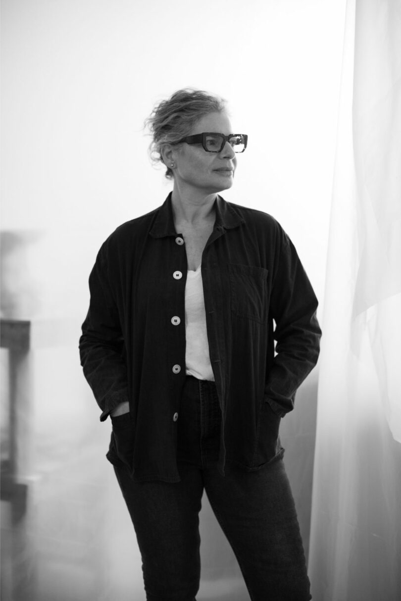 Portrait of artist Dana Harel standing in a softly lit studio environment.