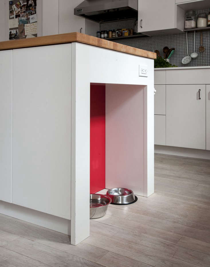 A minimalist white kitchen island featuring a built-in floor-level niche for pet water and food bowls.