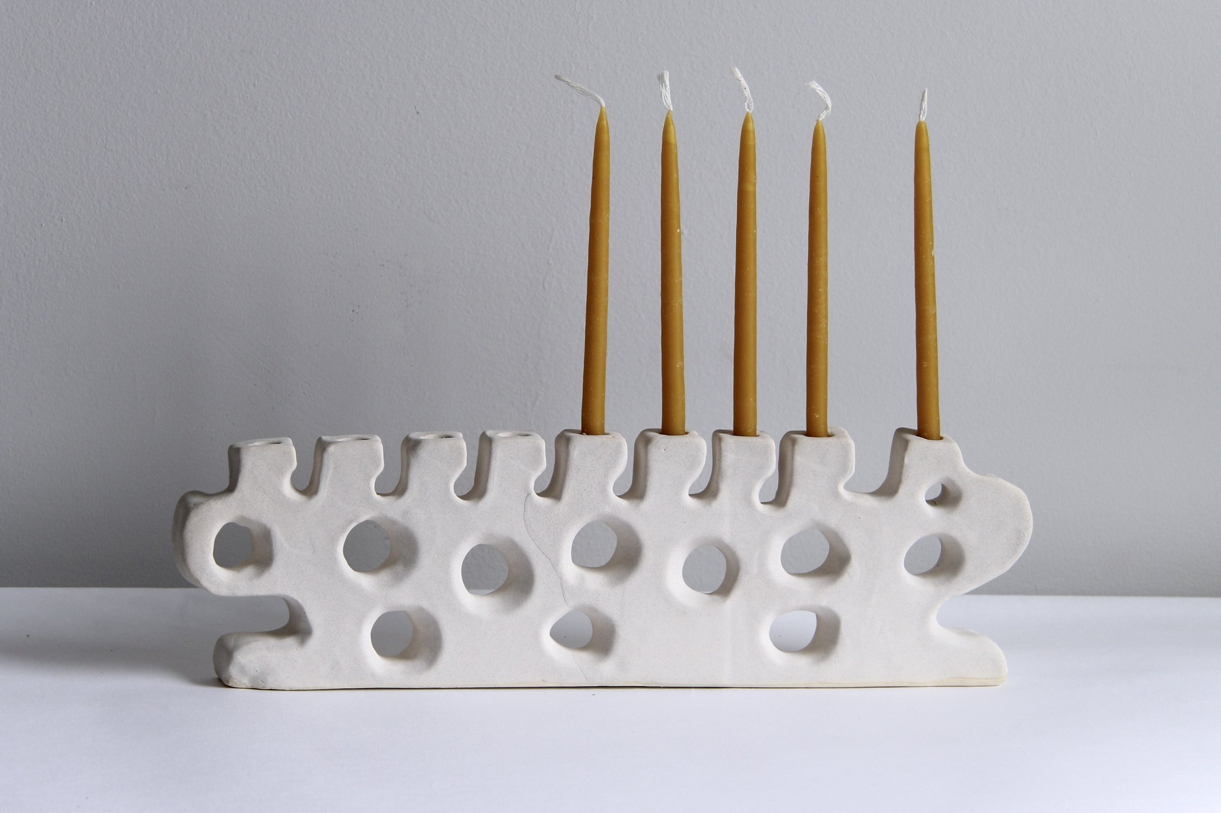 A hand-built ceramic menorah by ANK Studios featuring organic shapes and a light glaze.