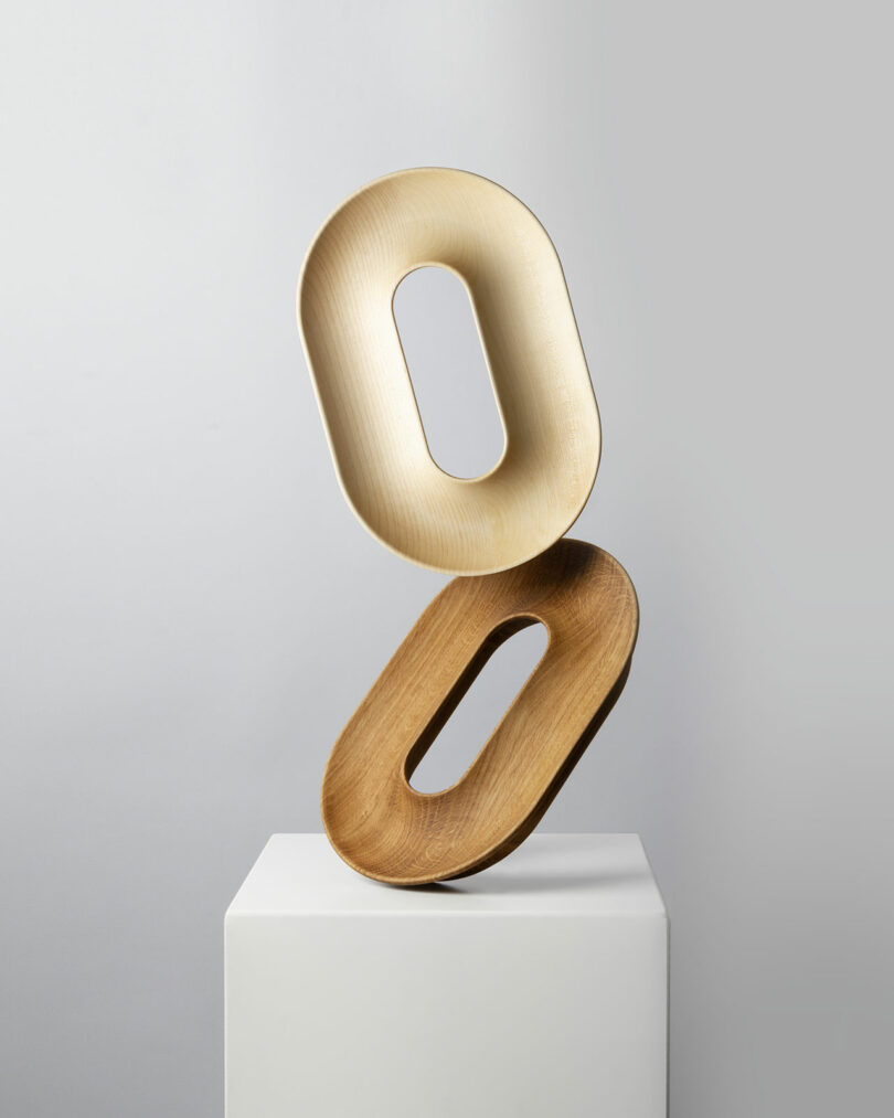 Two fruit vessels balanced vertically on a white pedestal against a gray background.