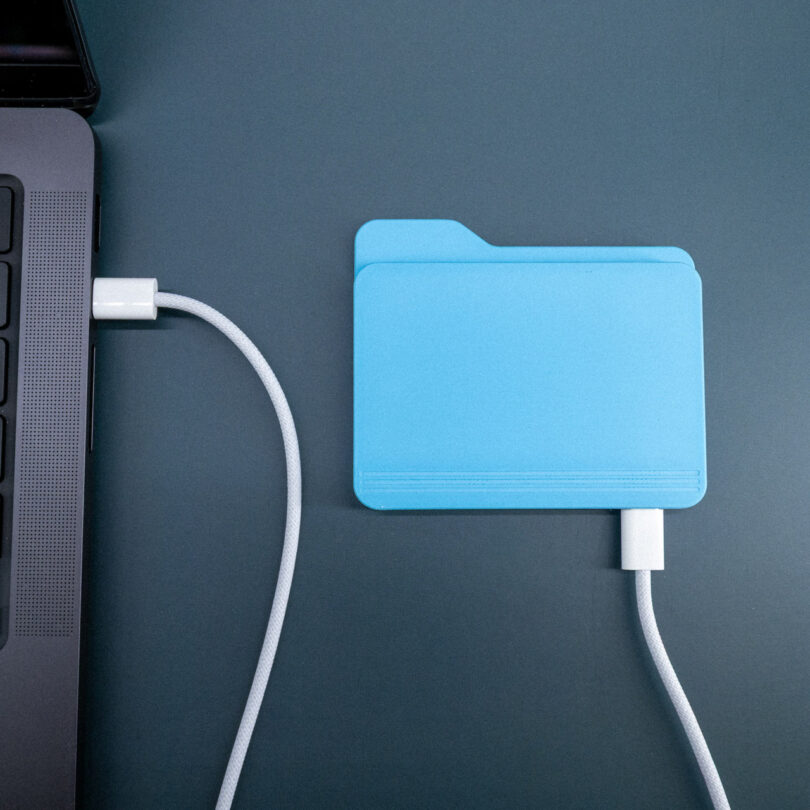 The FolderDrive connected to a MacBook Pro via a white USB-C cable on a professional dark desk surface.