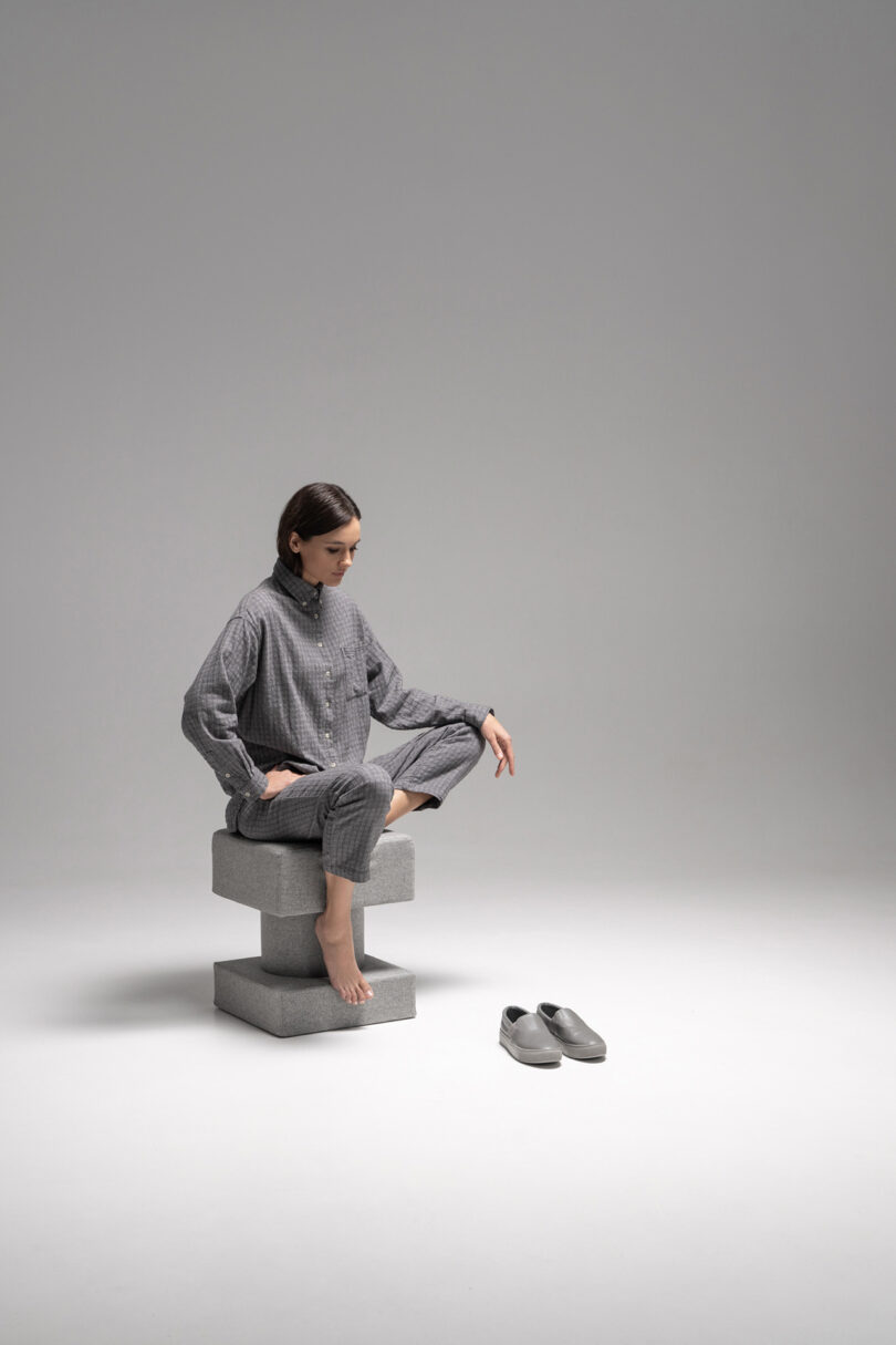 A woman in gray loungewear sits cross-legged on a stack of gray TAITŌ blocks.