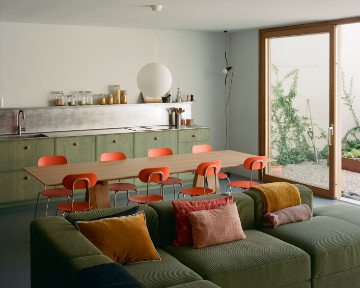 A long, minimalist kitchen unit stretching along a wall next to a large open living area with blue flooring.