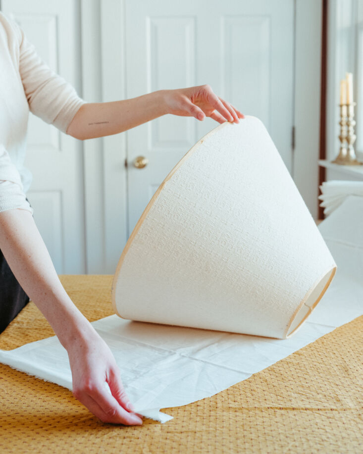 A person measuring a long strip of white fabric with a wooden yardstick.