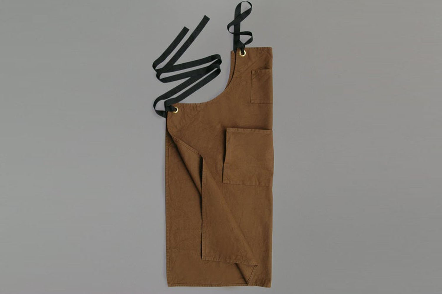 A caramel-colored heavy cotton duck bib apron with a front pocket.