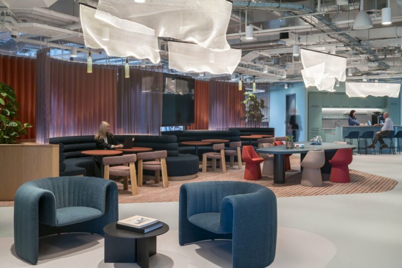 A modern lounge with blue chairs, round tables, and cloud-like light fixtures near a bar area.