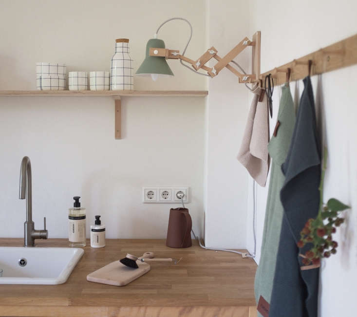 A wooden accordion-style wall light called Pixoss XL providing warm task lighting over a kitchen counter.