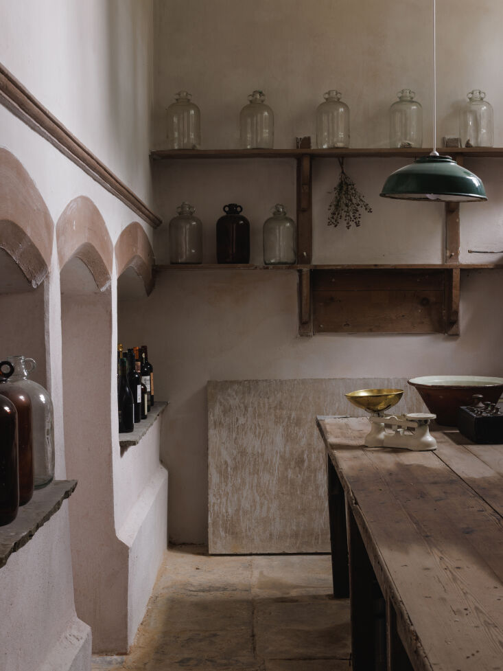 A pantry area with soft blue lime-washed walls, shelves of Kilner jars, and stone flooring.