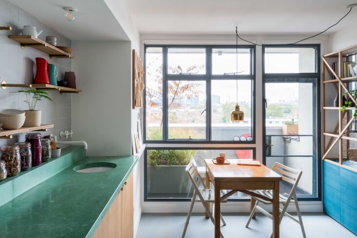 A warm and colorful modern kitchen interior with wooden elements inside a Brutalist building.