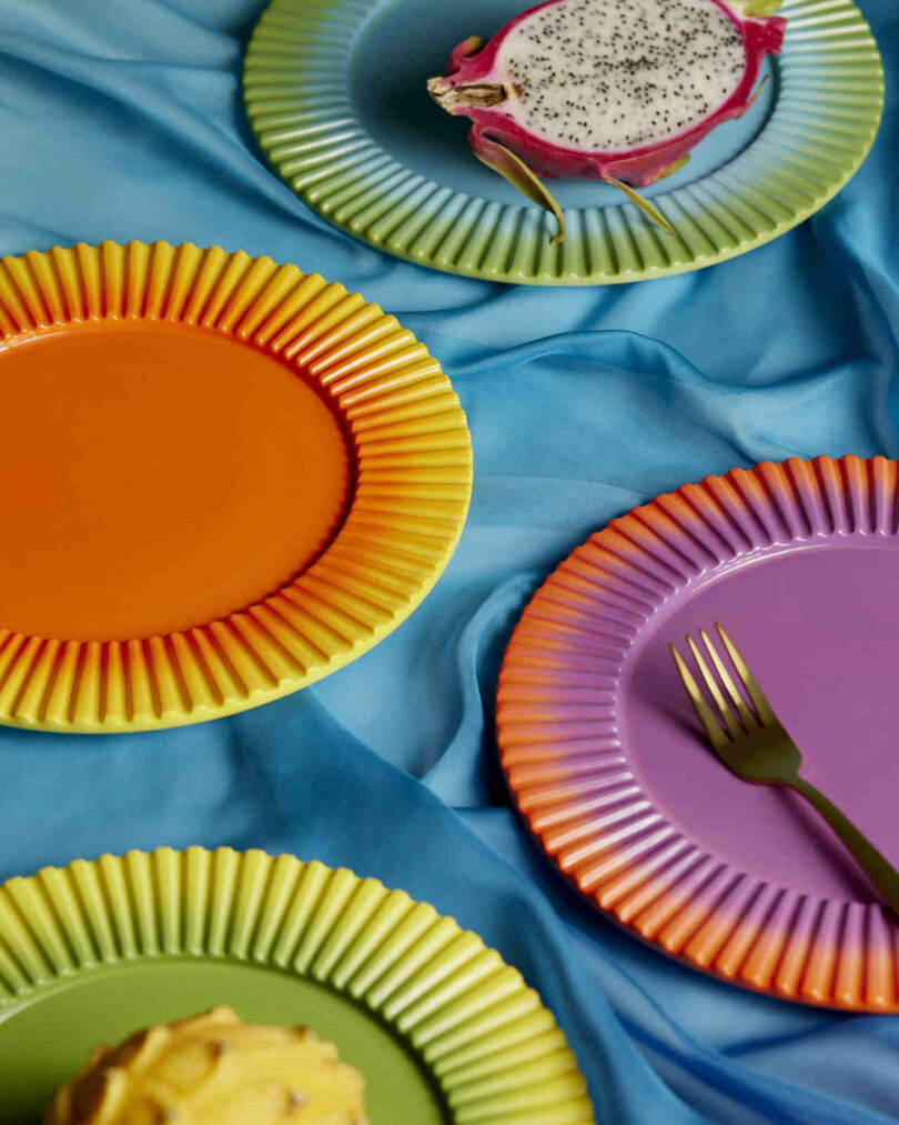 Close-up of vibrant gradient plates on a blue fabric background with sliced fruit.
