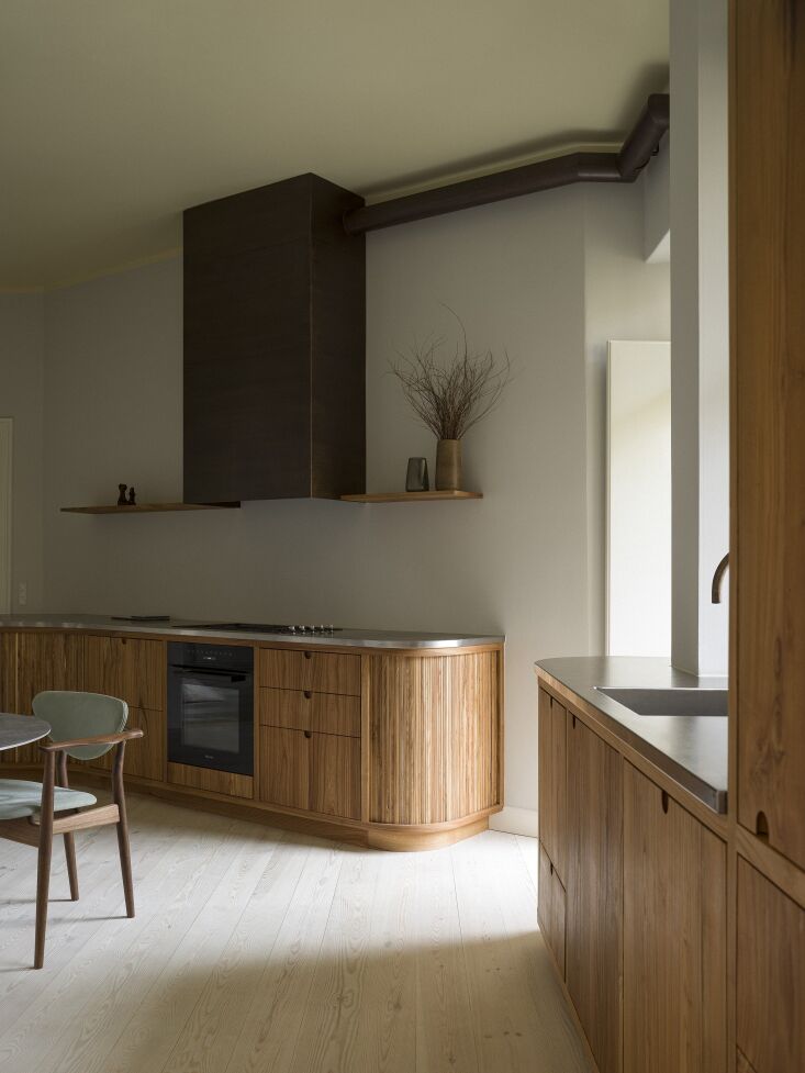 A custom burnished brass range hood paired with organic, half-round milled cabinet handles.