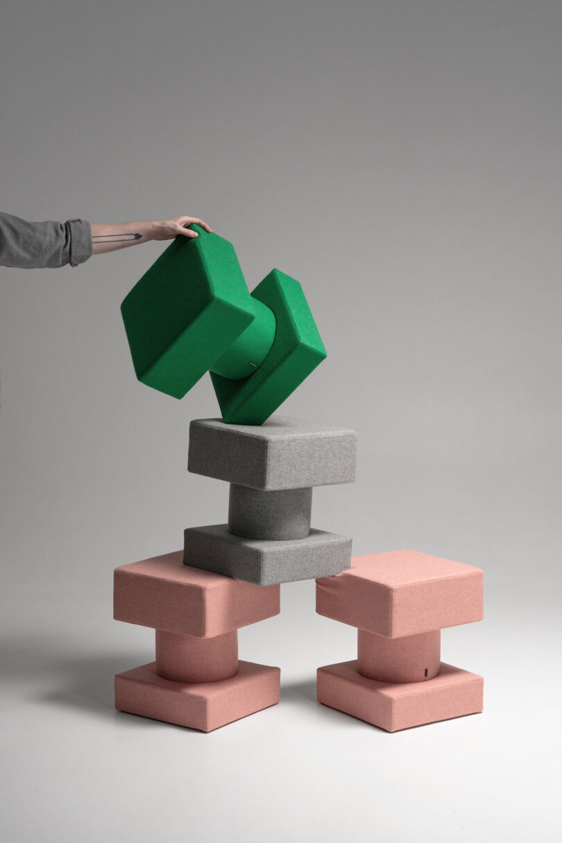 A hand placing green foam blocks onto a stack of gray and pink square blocks to show balanced construction.