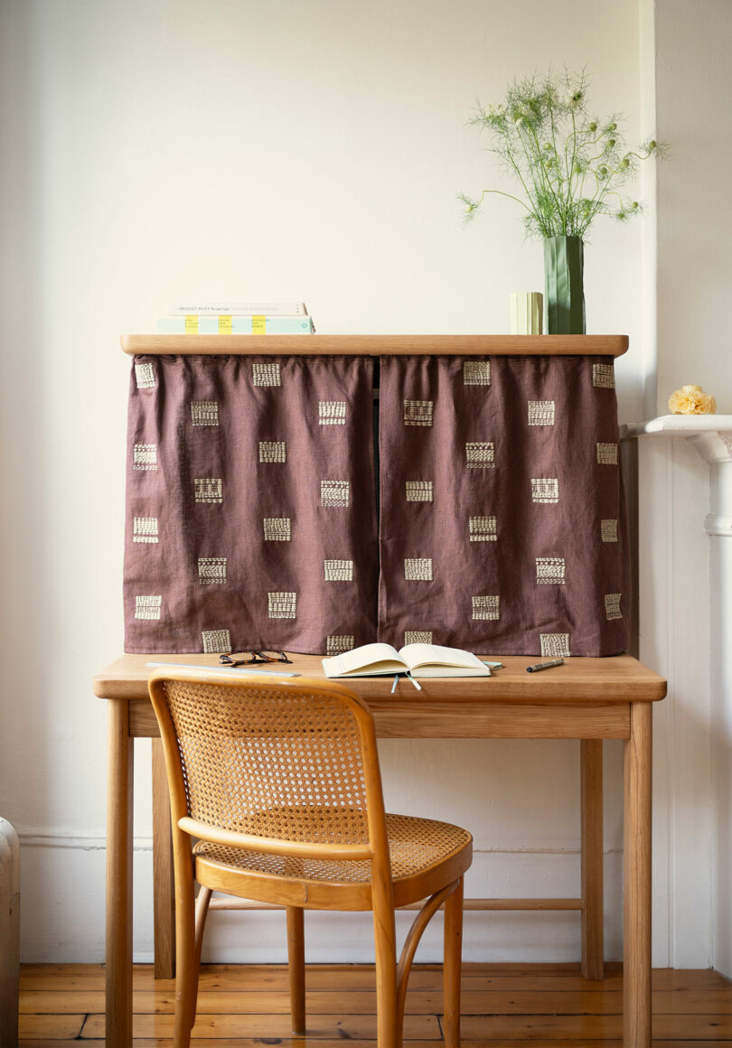 A wooden desk with a cane chair and a shelf partially covered by a patterned fabric screen.