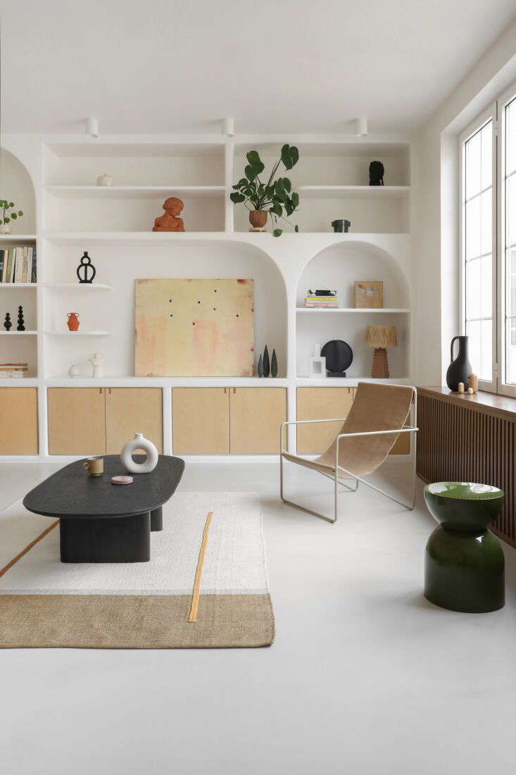 Open-plan living room featuring white limewash walls, built-in shelving, and a Ferm Living sling chair.