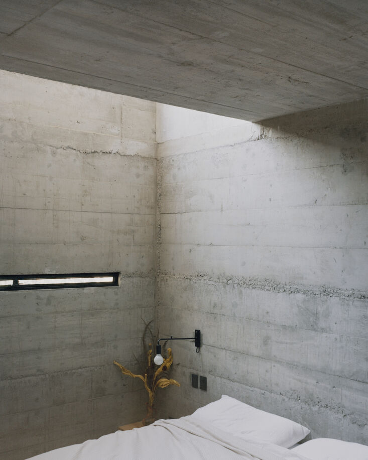 An artful, narrow vertical window in a raw concrete bedroom, casting a sliver of light.