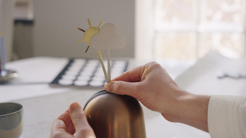 A person's hands placing a sun and cloud cutout onto the Skymill device.