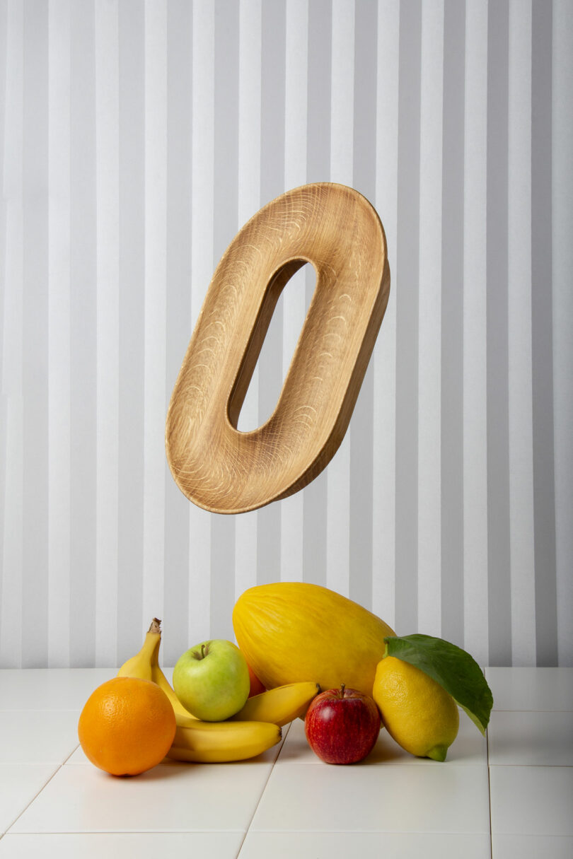 A wooden CIRCUIT fruit vessel with various fruits like bananas and oranges against a striped background.