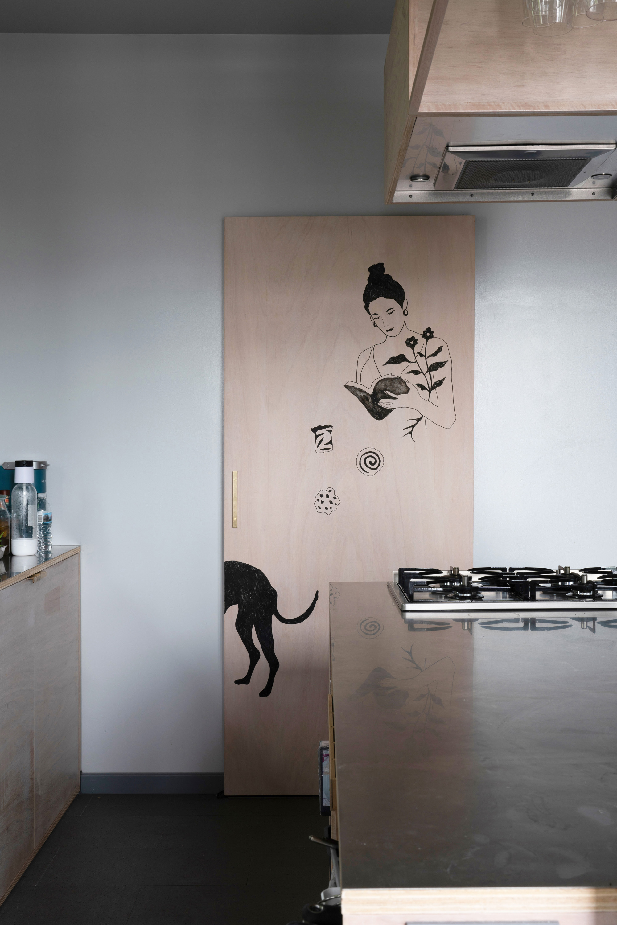 Black ink illustrations by a local artist on a birch plywood wall panel within the home-café.