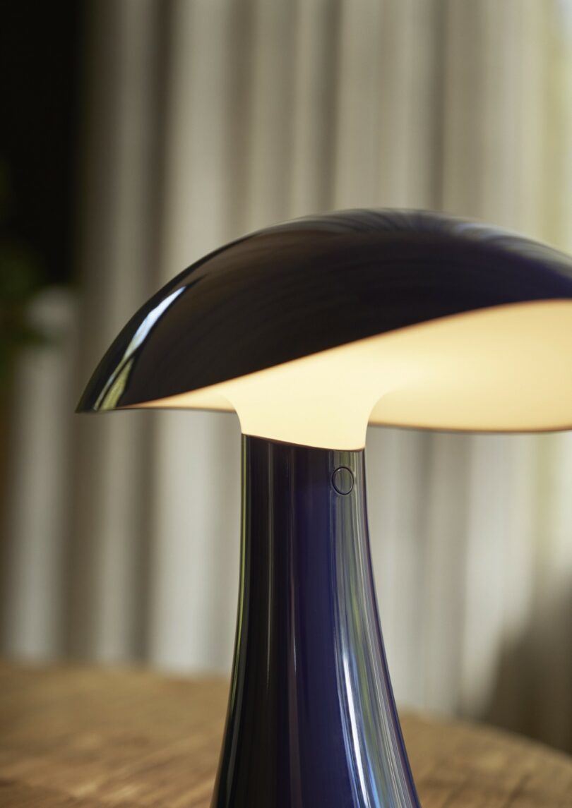 Close-up of a dark Rumee lamp with a curved shade illuminated on a wooden surface.