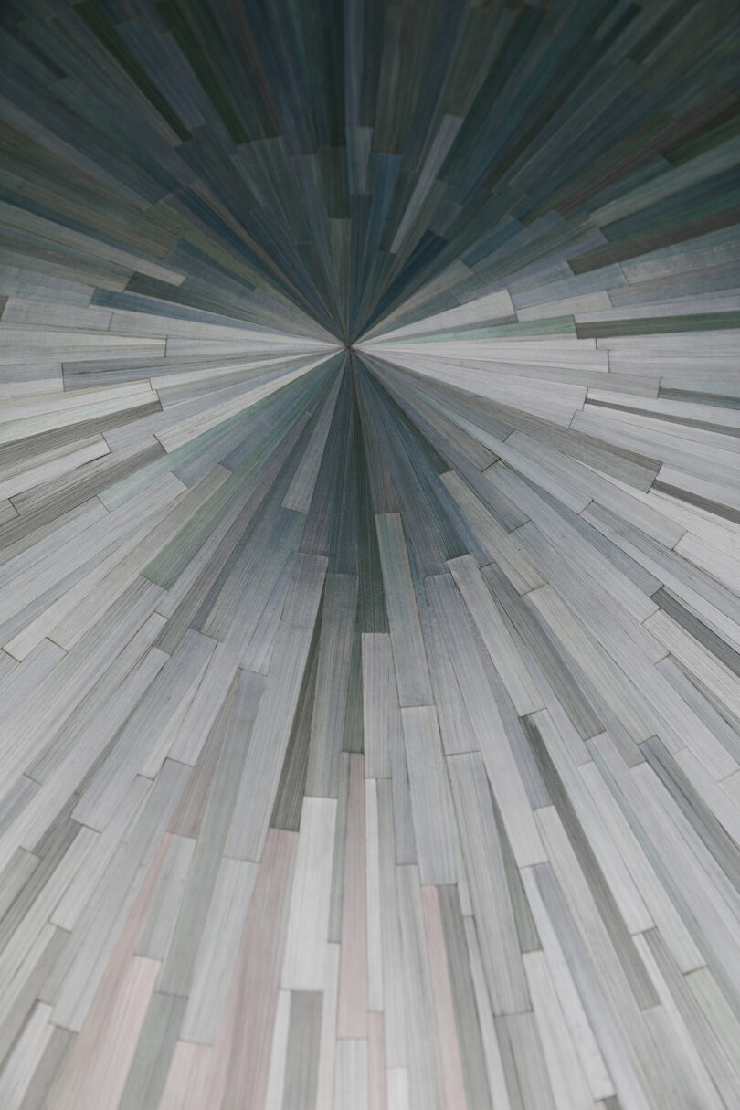 Top-down close-up of a radial geometric pattern with straw-like tiles radiating from a center point.
