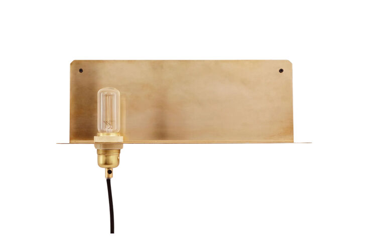 A minimalist brass L-shaped wall shelf with an exposed light bulb.