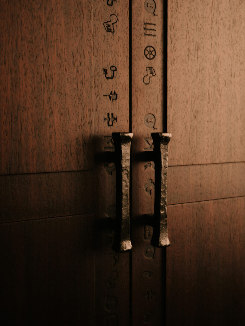 Close-up of metal handles on a wooden cabinet with engraved vertical symbols.