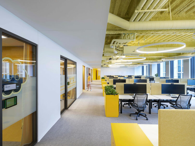 Open-plan office area with yellow accents, modern workstations, and glass meeting rooms.