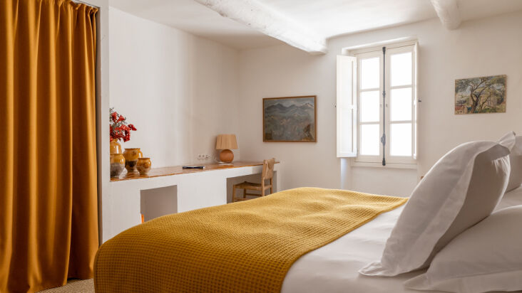 A hotel bedroom with sisal-clad walls, a built-in bed niche, and shuttered windows.