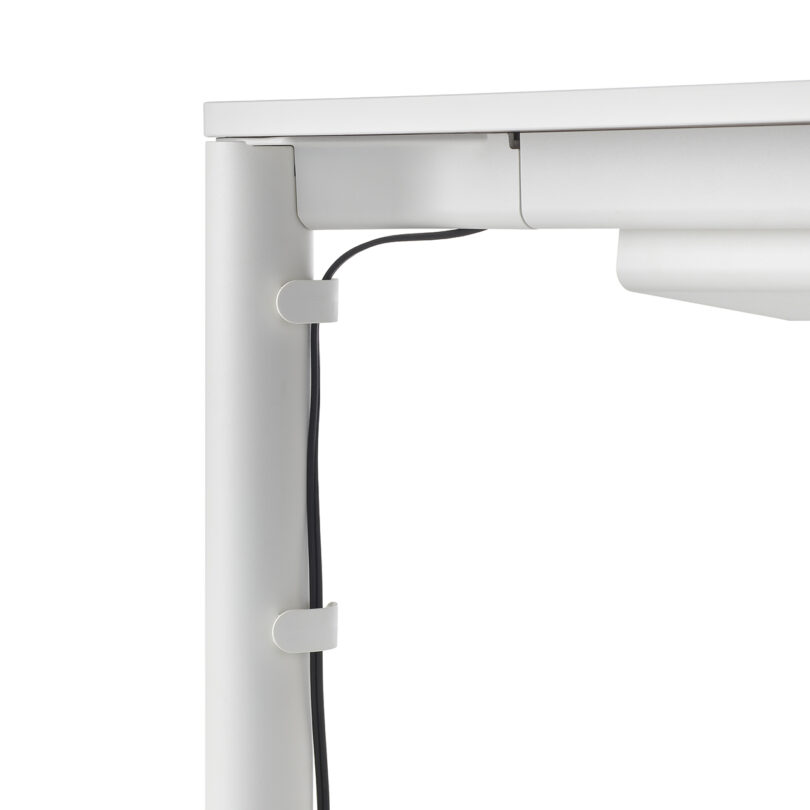 Detailed view of cable management clips securing a black wire to the white leg of a desk.