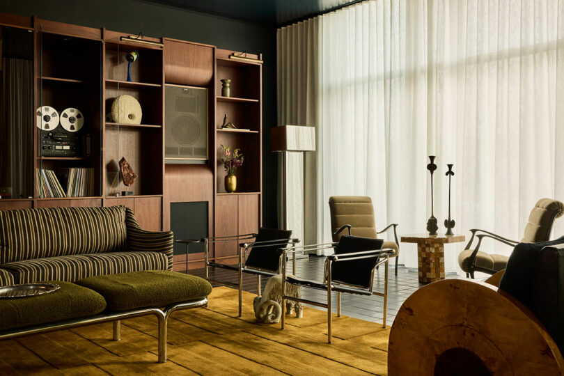 A mid-century modern living area with a striped green sofa, glass coffee table, and floor-to-ceiling sheer curtains.
