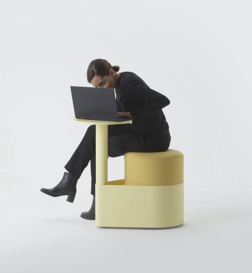 User working on a laptop using the yellow pony chair's integrated tabletop.